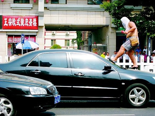 The woman loosens her high heeled shoe from the crushed windshield of a black Honda.